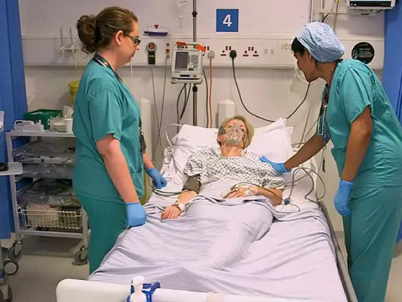 A patient laying in a bed, in theatre recovery. Surgeons in scrubs are stood at the patients bed side.