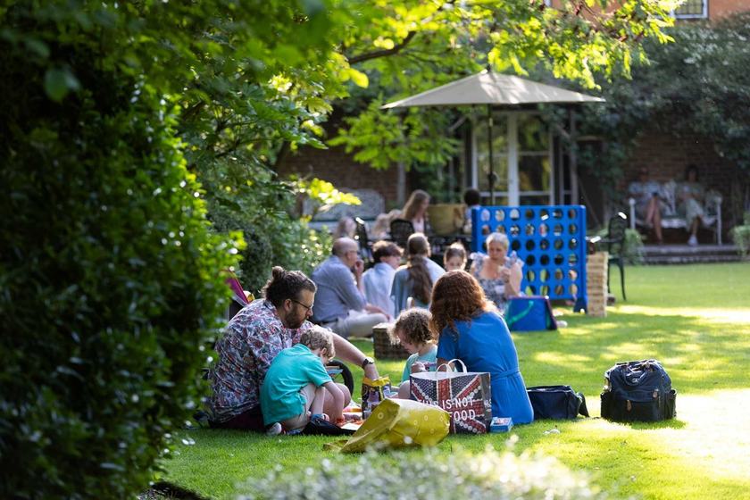 Groups of adults and children enjoying picnics on a lush lawn in a beautiful garden