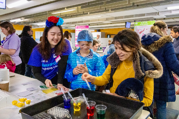 People standing in front of a lab bench holding pipettes in front of bright coloured glasses