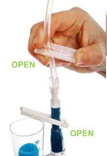 Hand opening a clear plastic clamp on medical tubing, with the word “OPEN” shown.